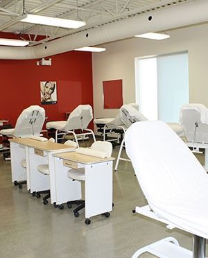 Nail salon or spa interior with manicure tables, massage beds, and a red accent wall.