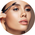 Woman brushes eyebrow with a spoolie brush; neutral setting.