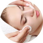Person receiving a facial. Hands holding cotton pads gently cleanse the face. Eyes are closed.