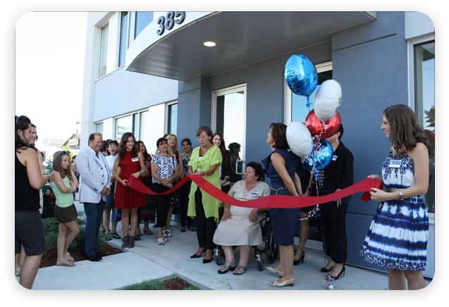 People cutting a red ribbon in front of a building with balloons.