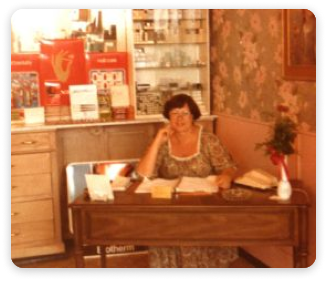 Woman at a desk with paperwork, seated in a room with a vintage floral wallpaper.