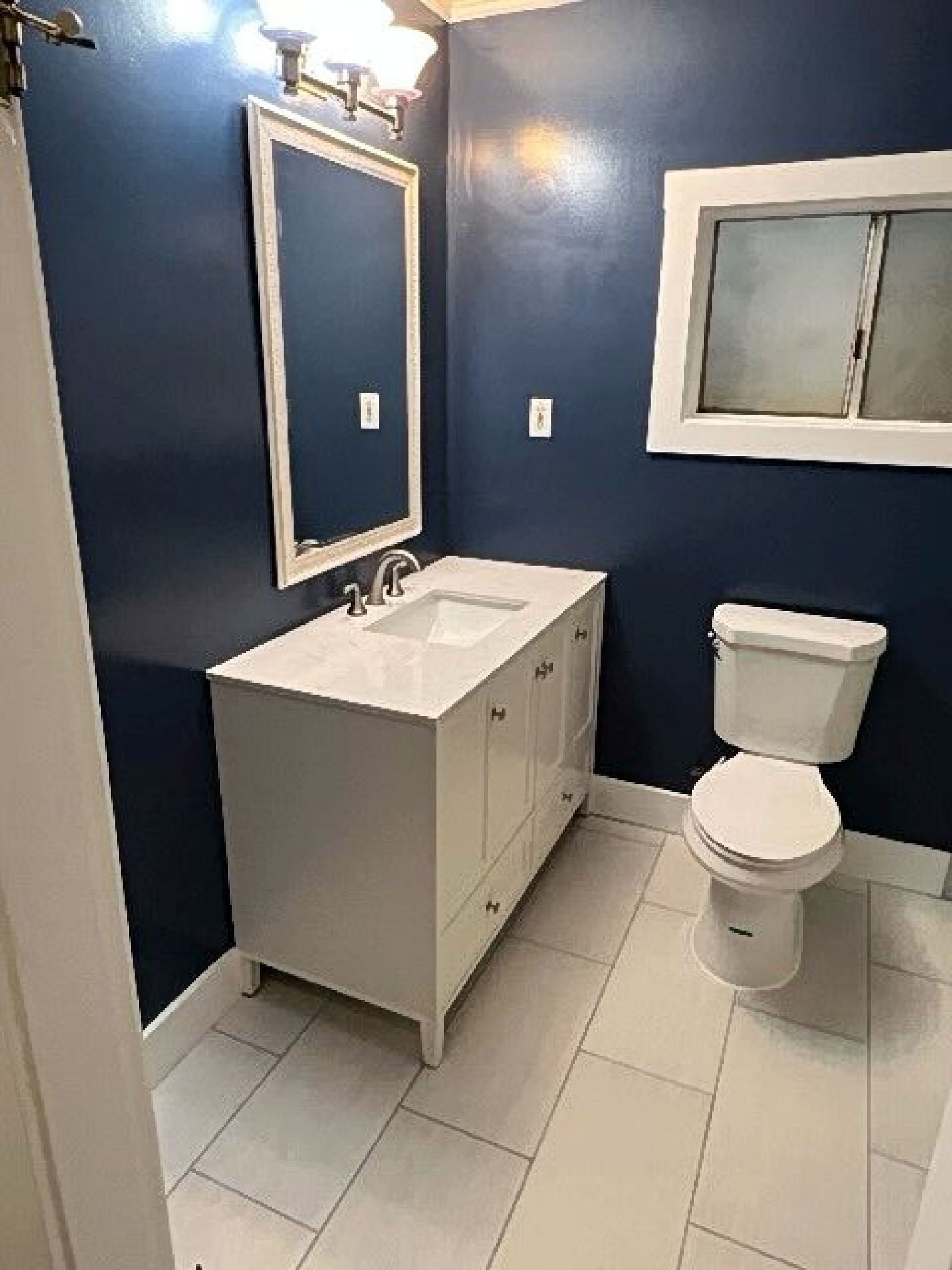 A bathroom with a sink , toilet , mirror and window.