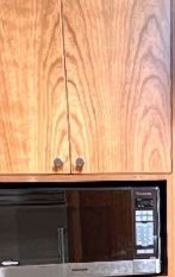A microwave oven is sitting under a wooden cabinet in a kitchen.