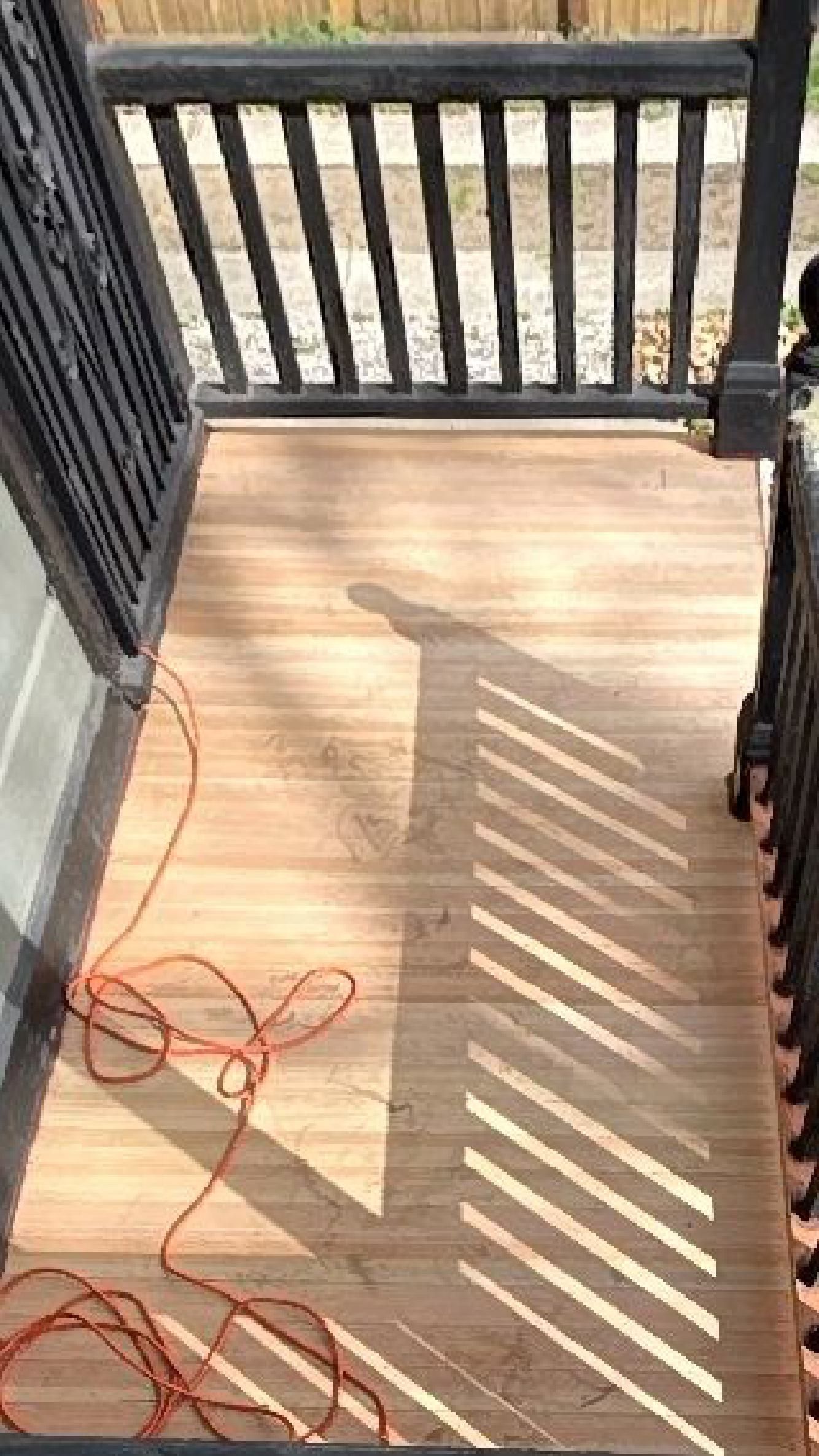 A wooden deck with a black railing and a power cord.