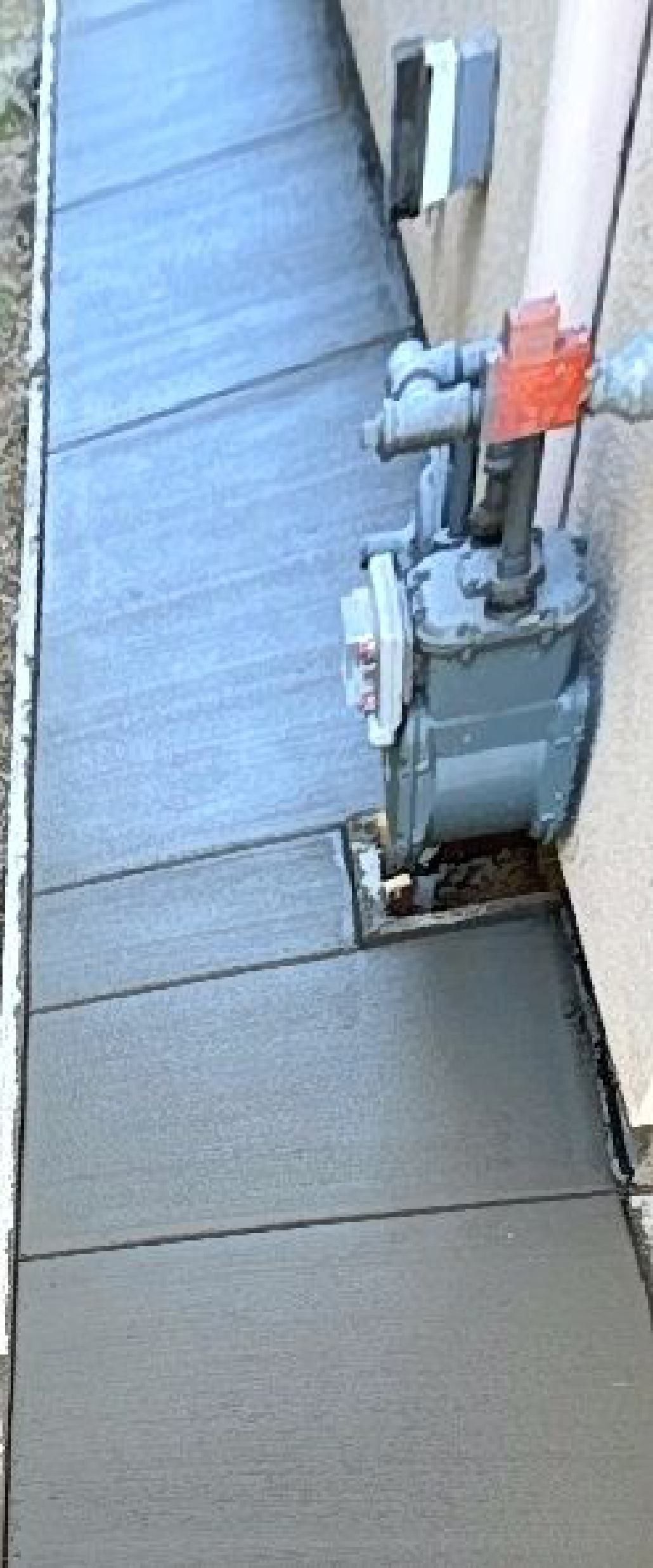 A sidewalk with a gas meter on the side of a building.