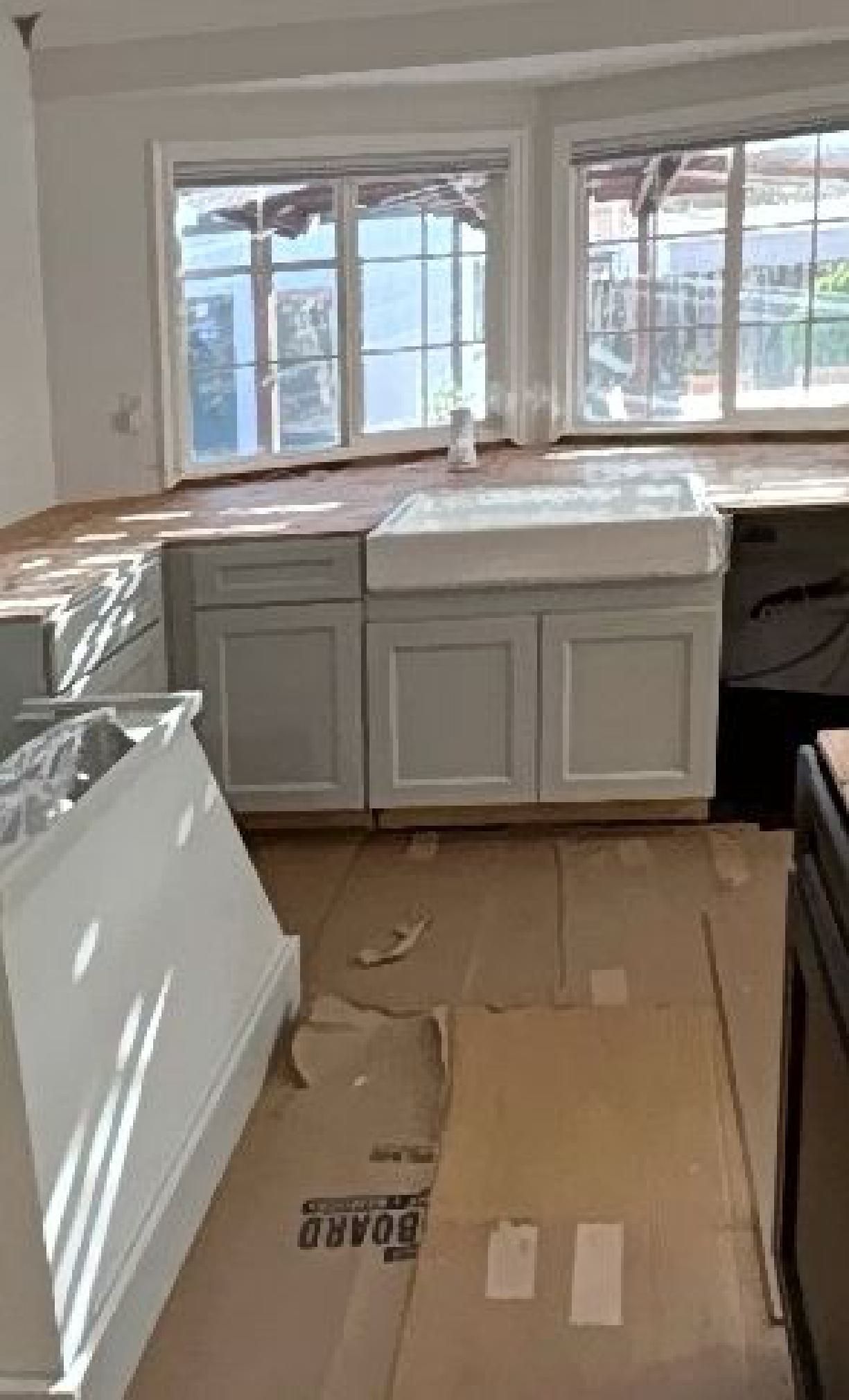 A kitchen with white cabinets , a sink , and a lot of windows.