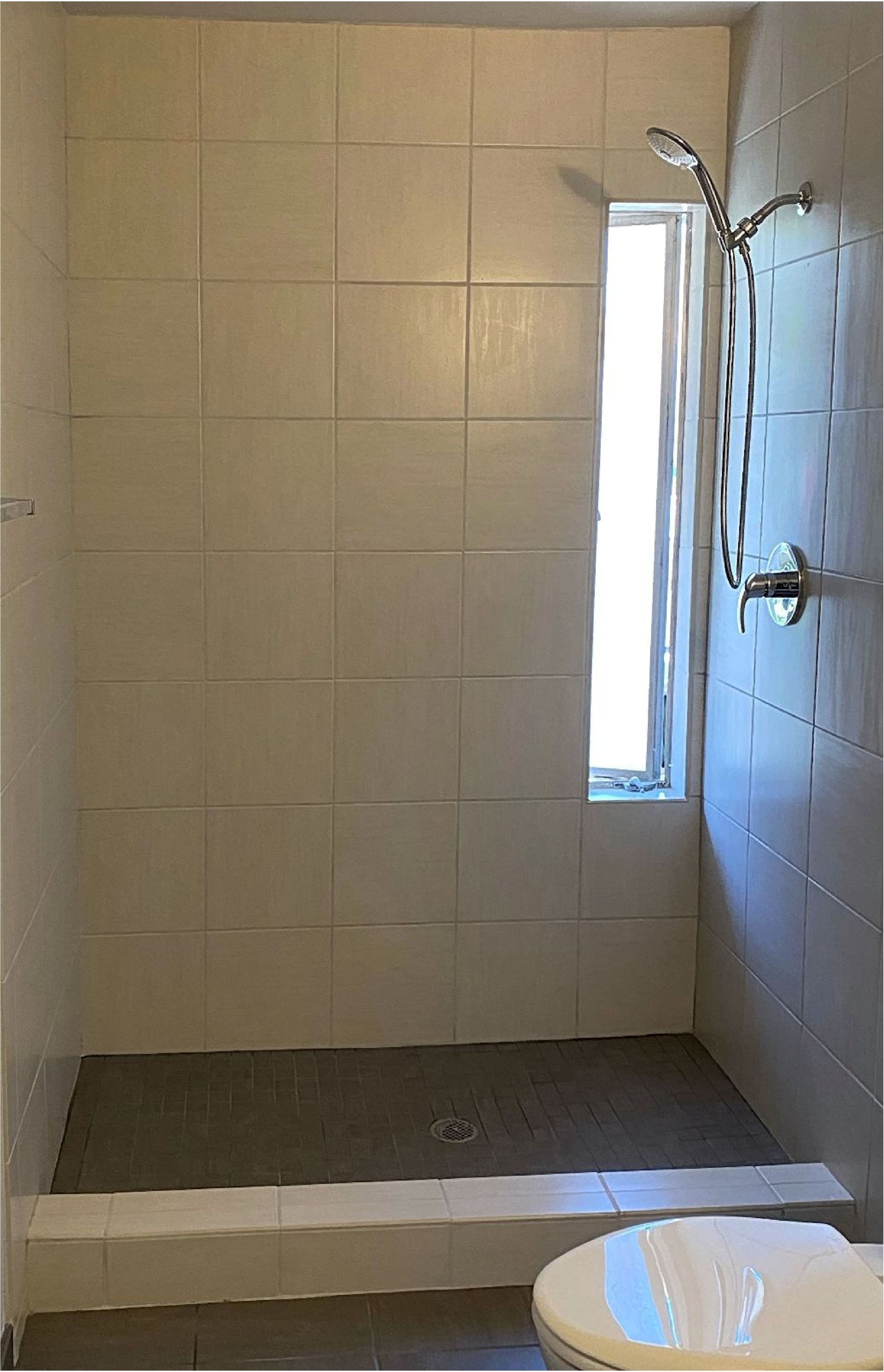 A bathroom with a toilet , shower , and window.