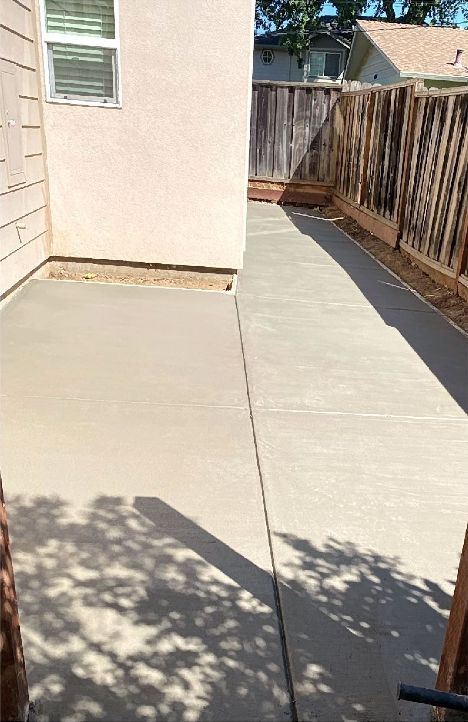 A concrete walkway leading to a house with a wooden fence.