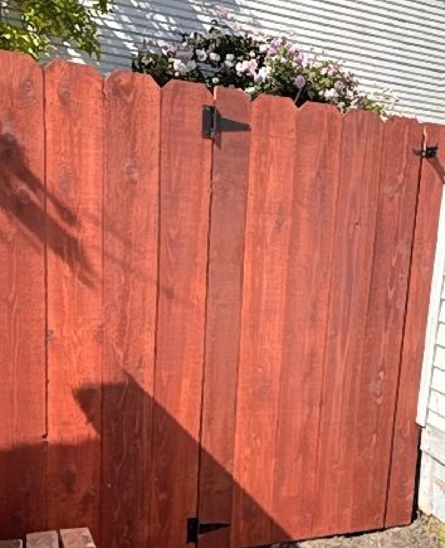 A red wooden fence with flowers in the background