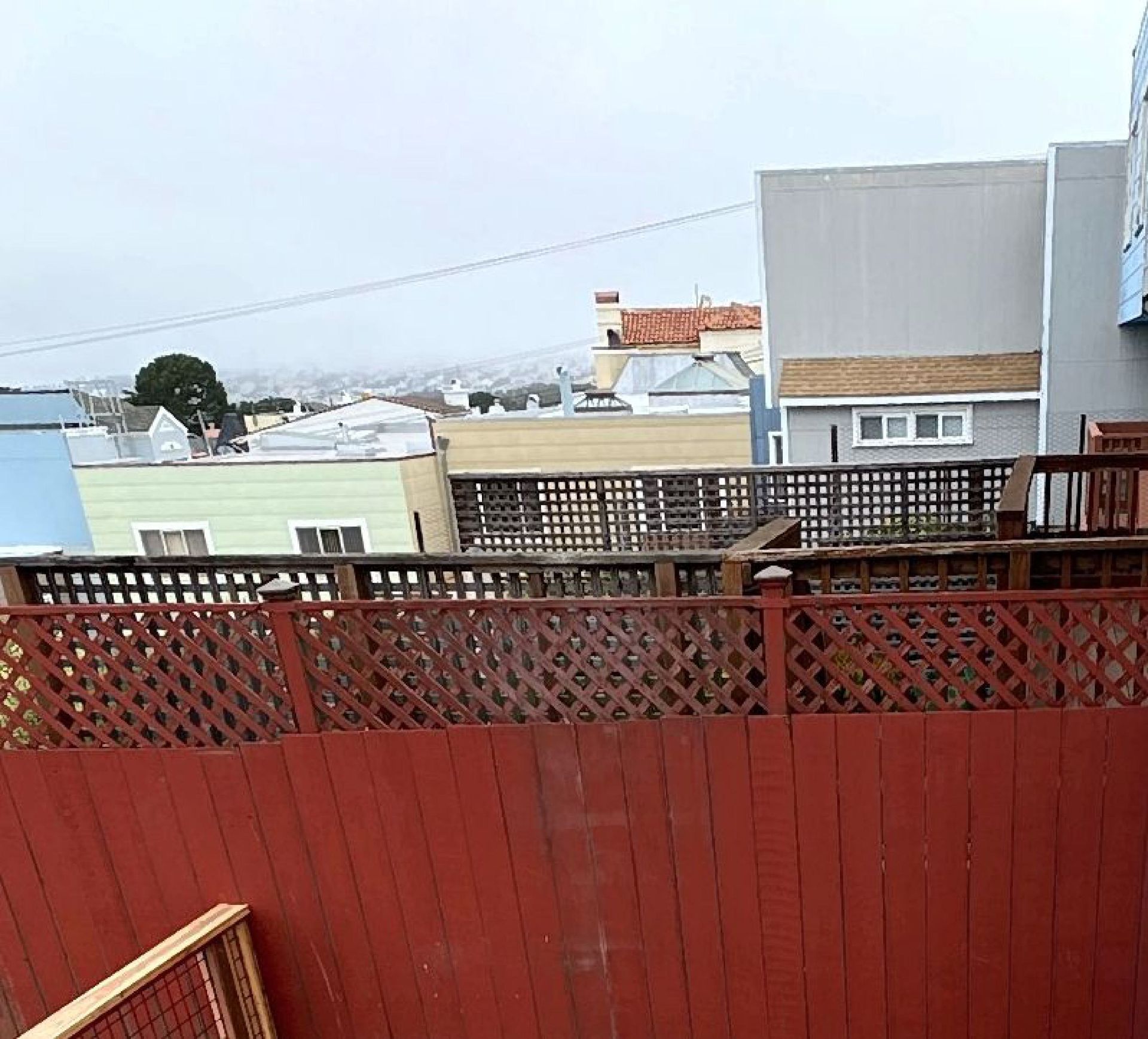A red fence surrounds a balcony with a view of a city.
