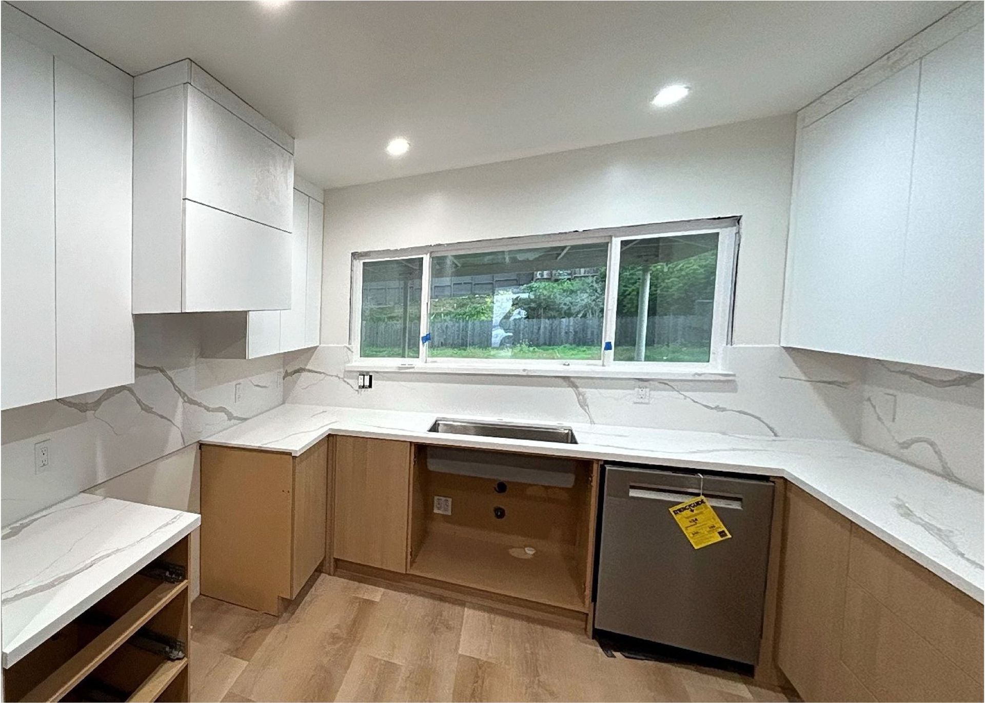 A kitchen with white cabinets , stainless steel appliances , and a large window.