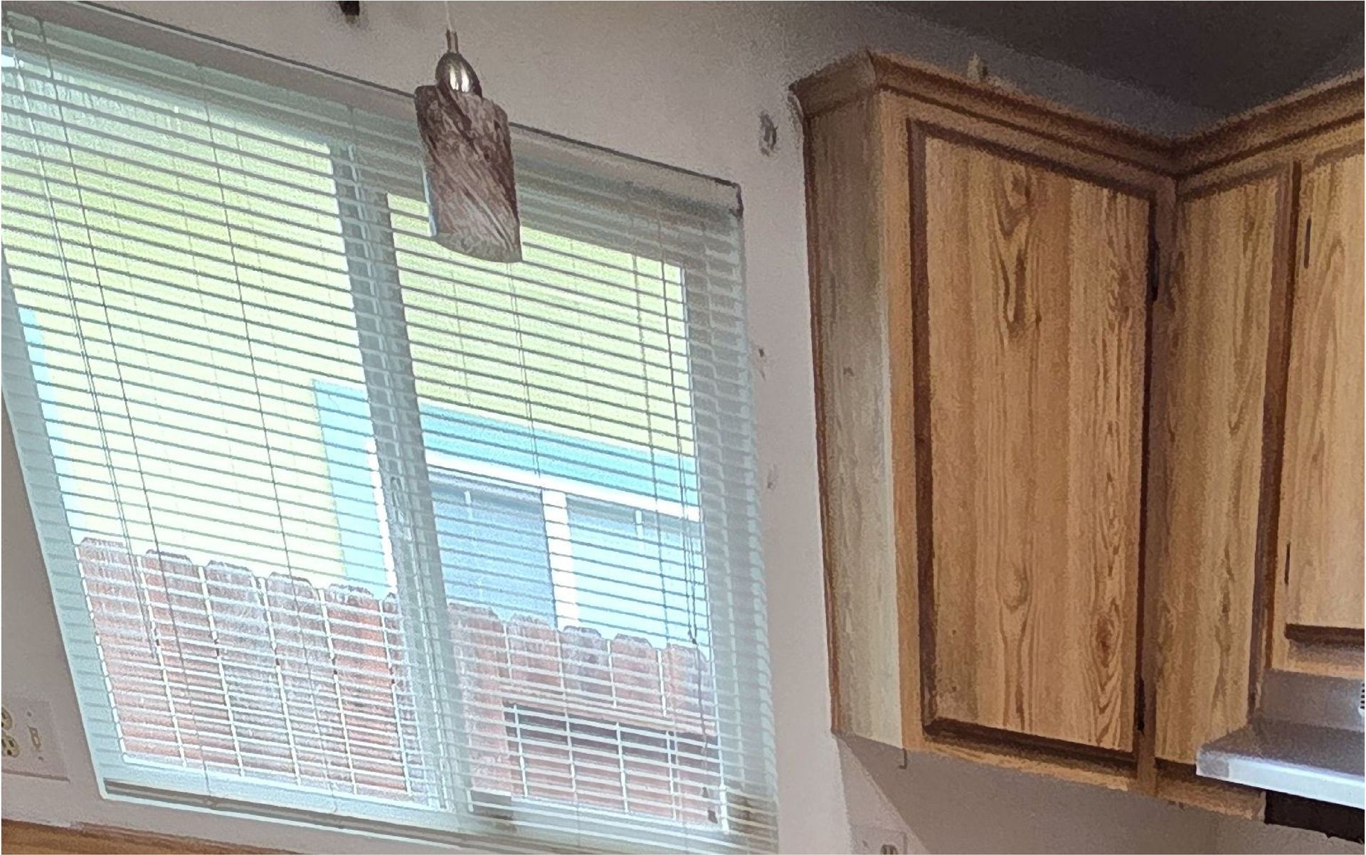 A kitchen with wooden cabinets and a window with blinds.