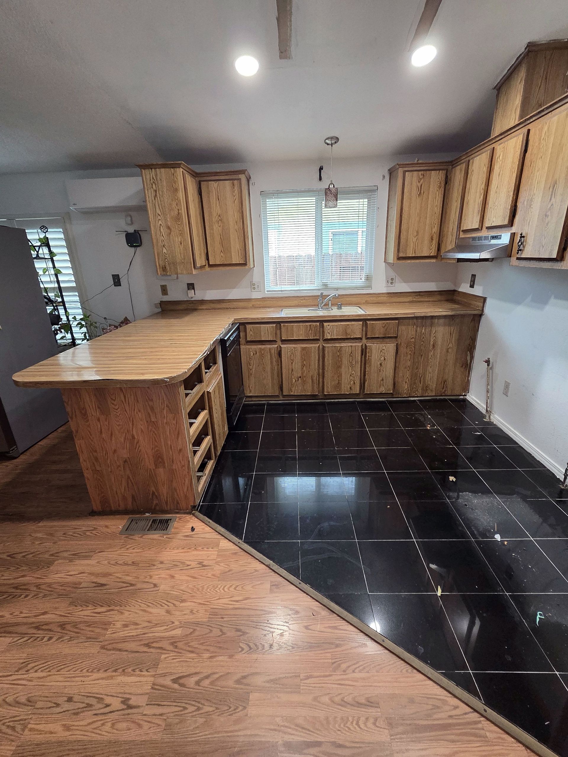 A kitchen with wooden cabinets and a black tile floor.