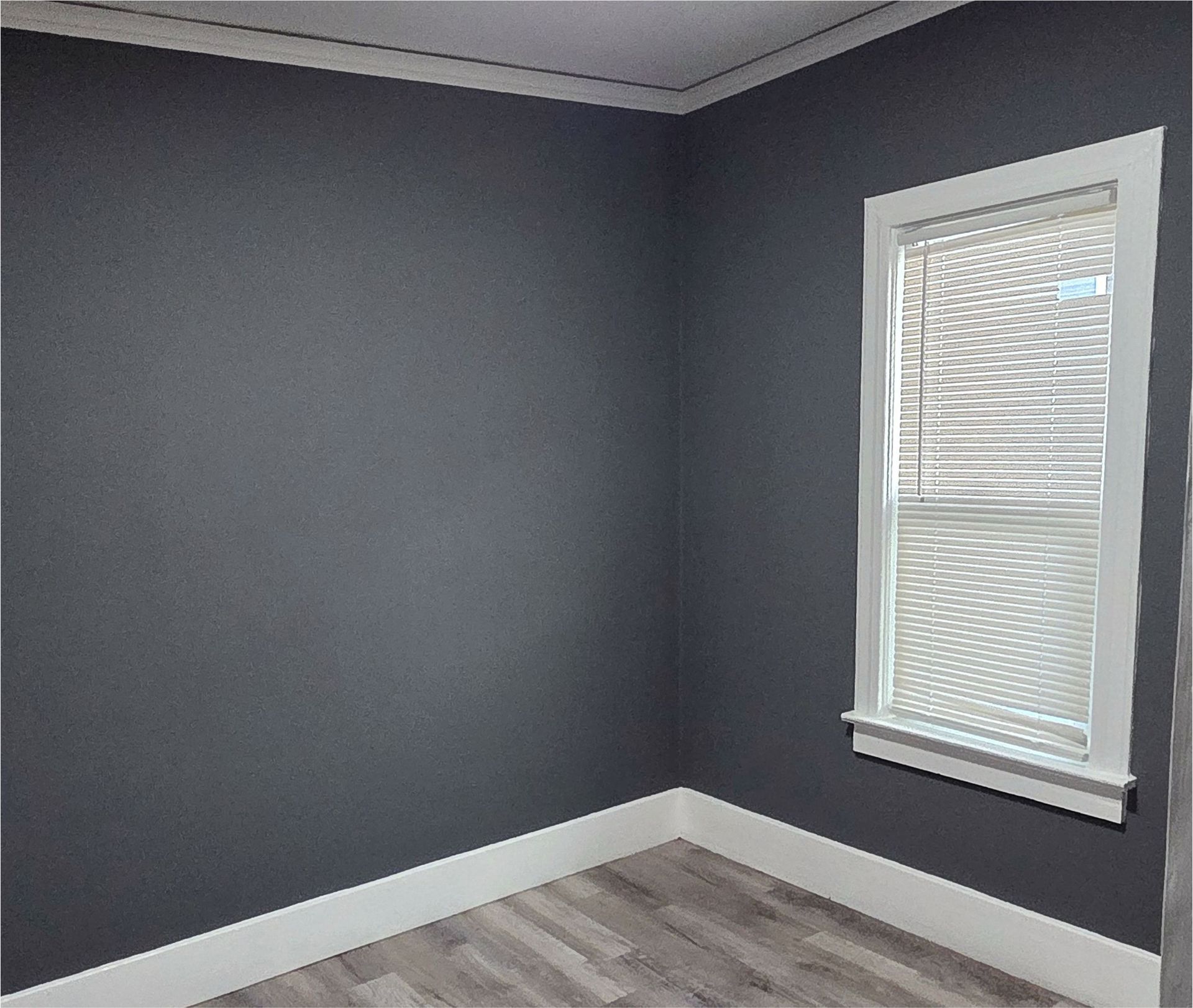 An empty room with gray walls and a window with blinds.