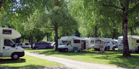 Aerial view of an industrial complex with blue-roofed buildings, a white-roofed warehouse, and trucks in a forested area.