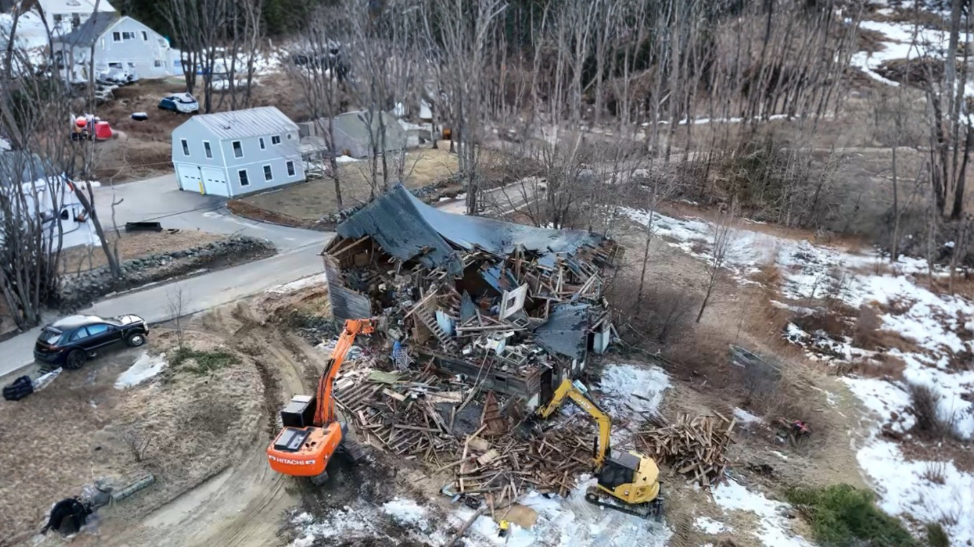Two excavators demolishing a barn, piles of debris scattered on the ground.