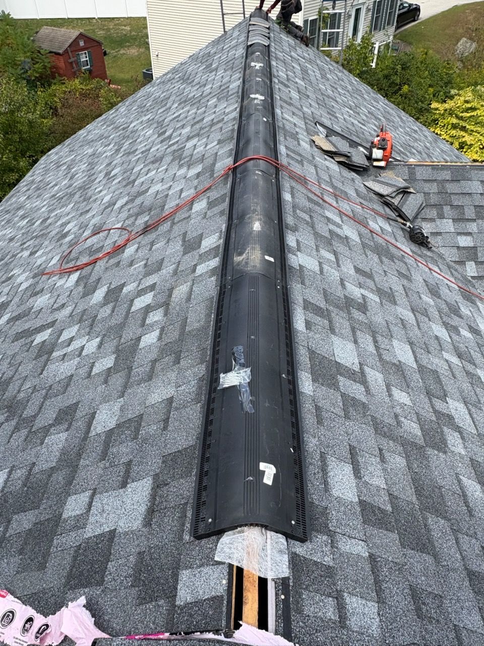 A man wearing an orange hard hat is working on a pipe in the attic.