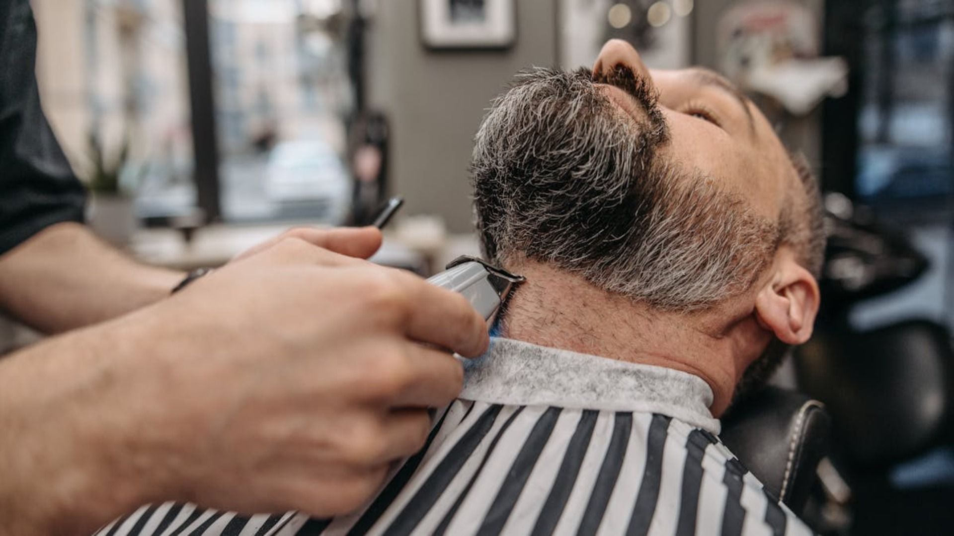 Un barbero corta el cuello de un cliente con una maquinilla en una barbería.