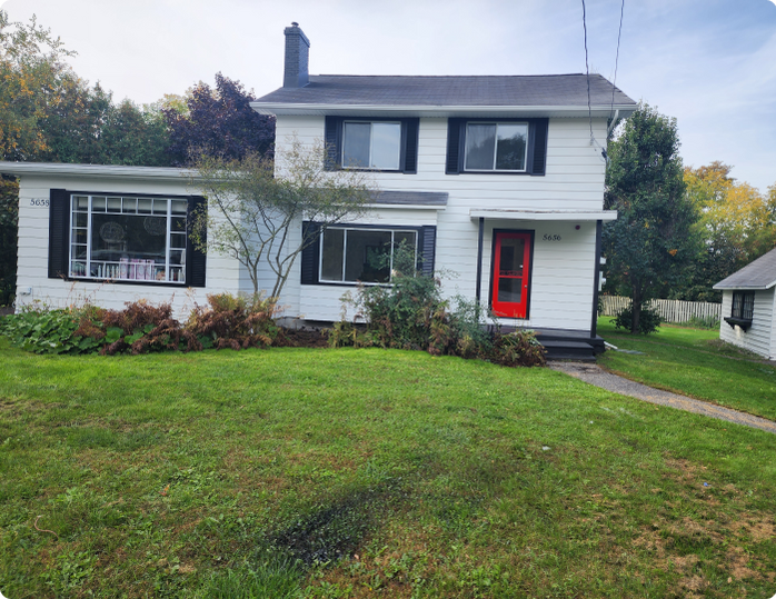 A white house with black shutters and a red door is sitting on top of a lush green lawn.