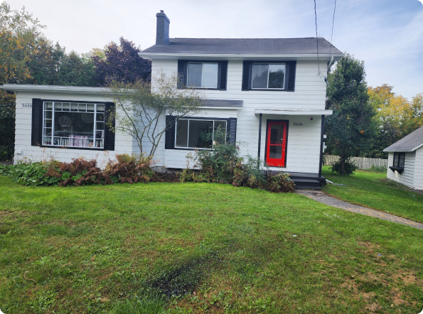A white house with black shutters and a red door is sitting on top of a lush green lawn.