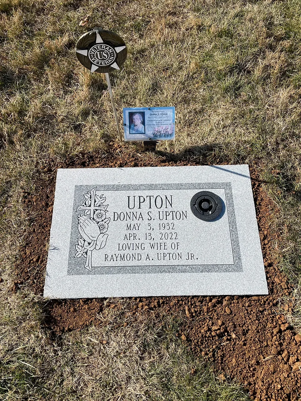 A light gray granite grave marker for the Upton family, featuring a small memorial photo and a circular metal vase.