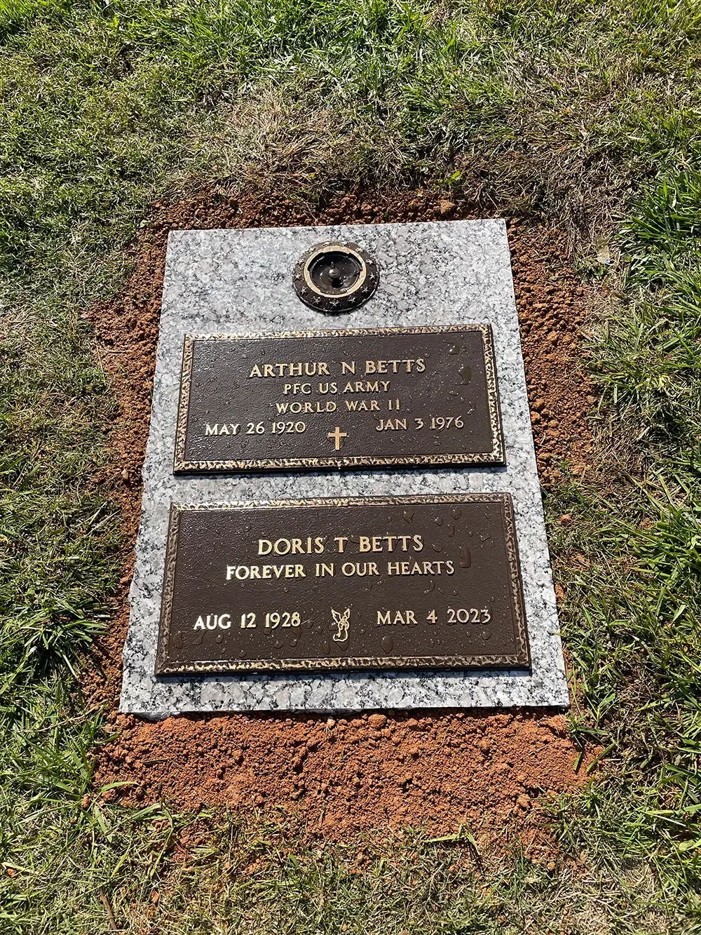 A bronze double-marker headstone on a light gray granite base set in grass, commemorating Arthur and Doris Bliss.