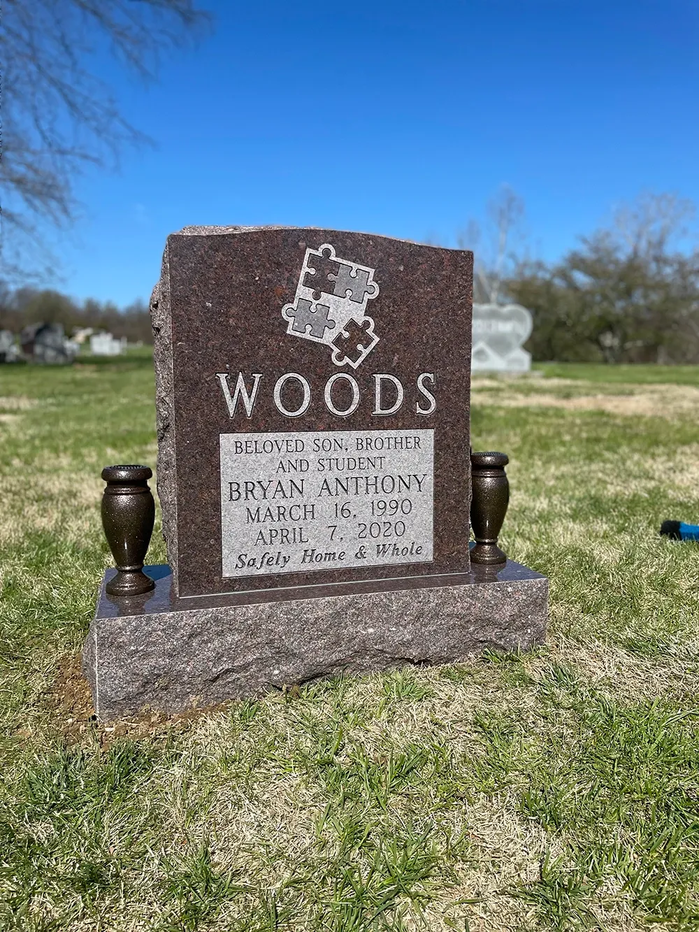 A granite headstone for the Woods family, featuring a puzzle piece engraving, located in a grassy cemetery.