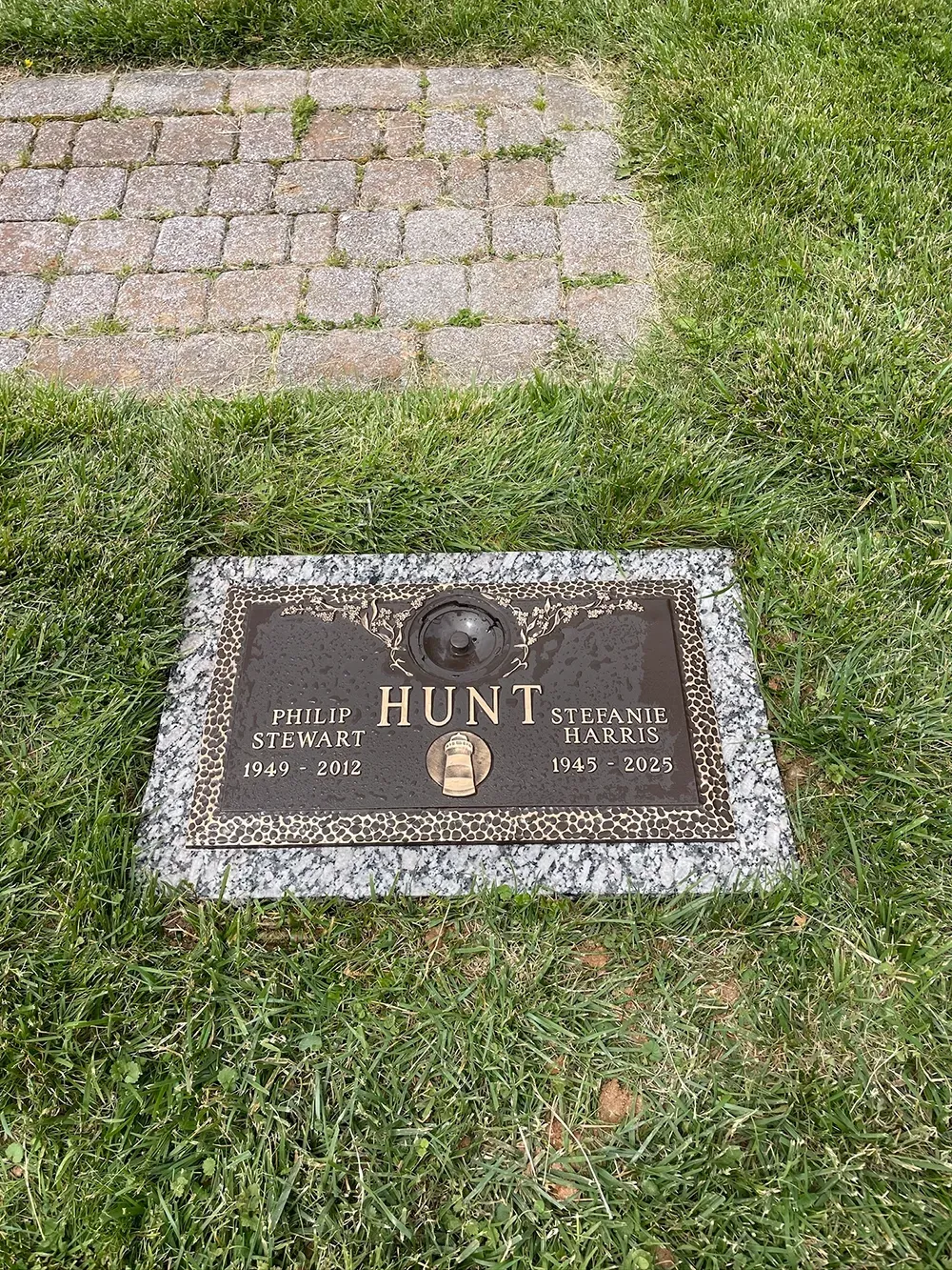 A bronze memorial plaque for the Hunt family set in a lawn, with names and dates inscribed below a central emblem.
