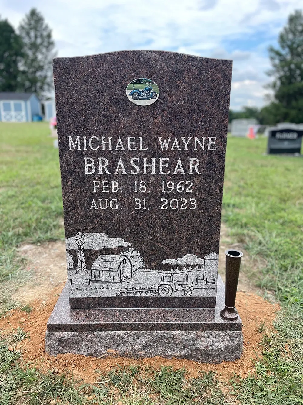 A granite gravestone for Michael Wayne Brashear, inscribed with his birth and death dates, in a grassy cemetery.