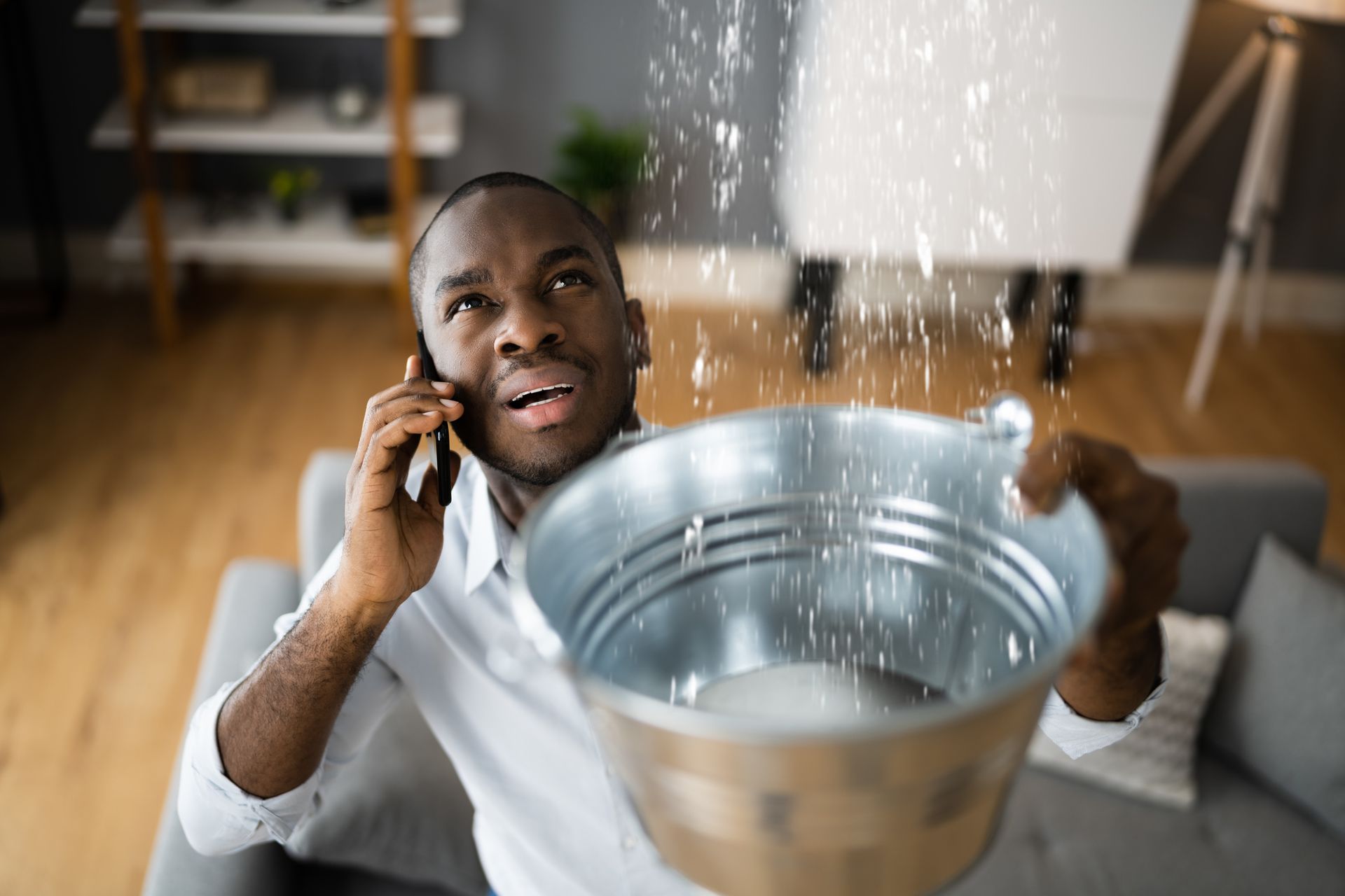 Man catches ceiling leak in bucket while calling for help on his phone. Man catches ceiling leak in bucket while calling for help on his phone.