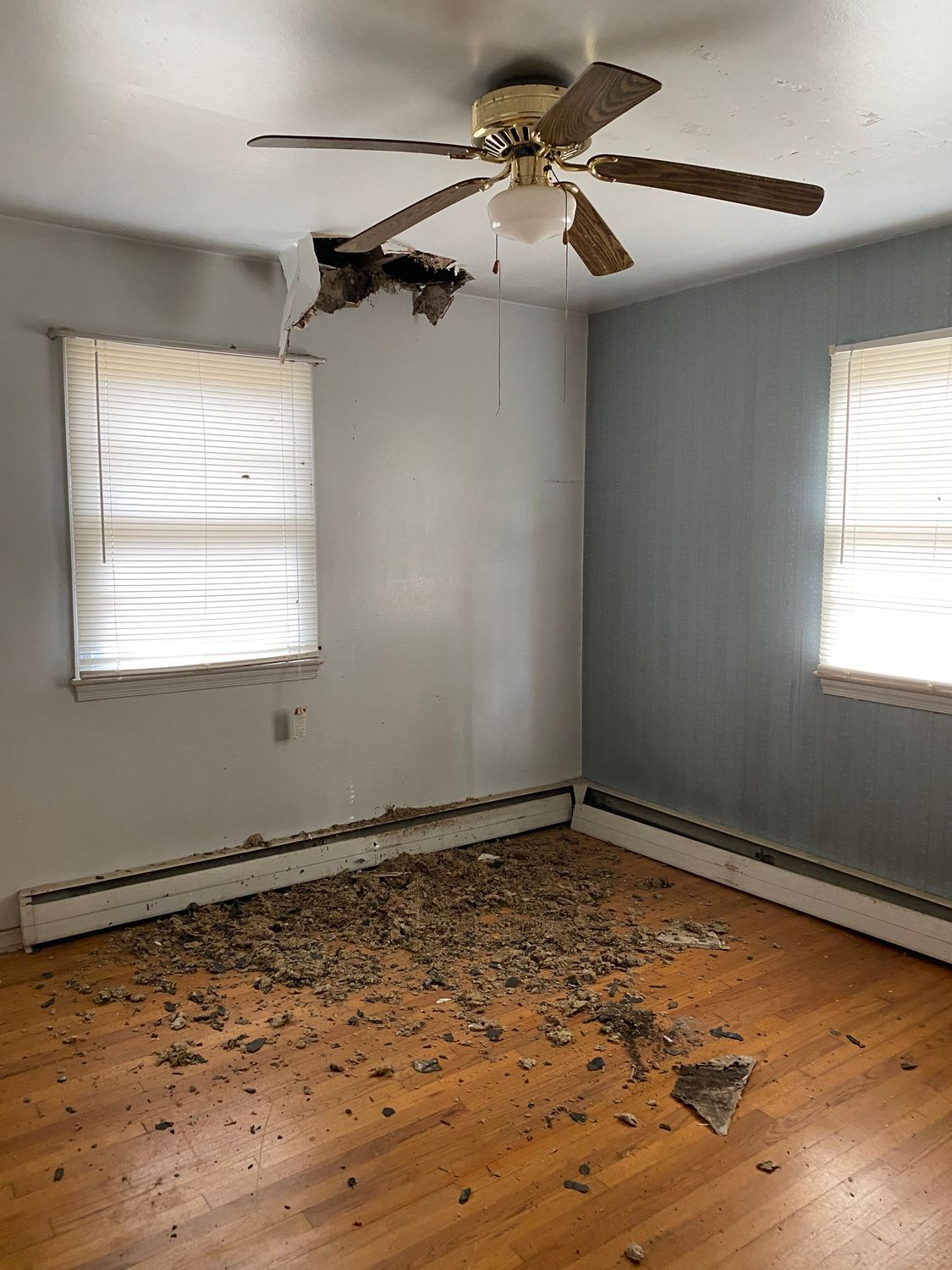 A room with a hole in the ceiling and debris on the floor caused by water damage