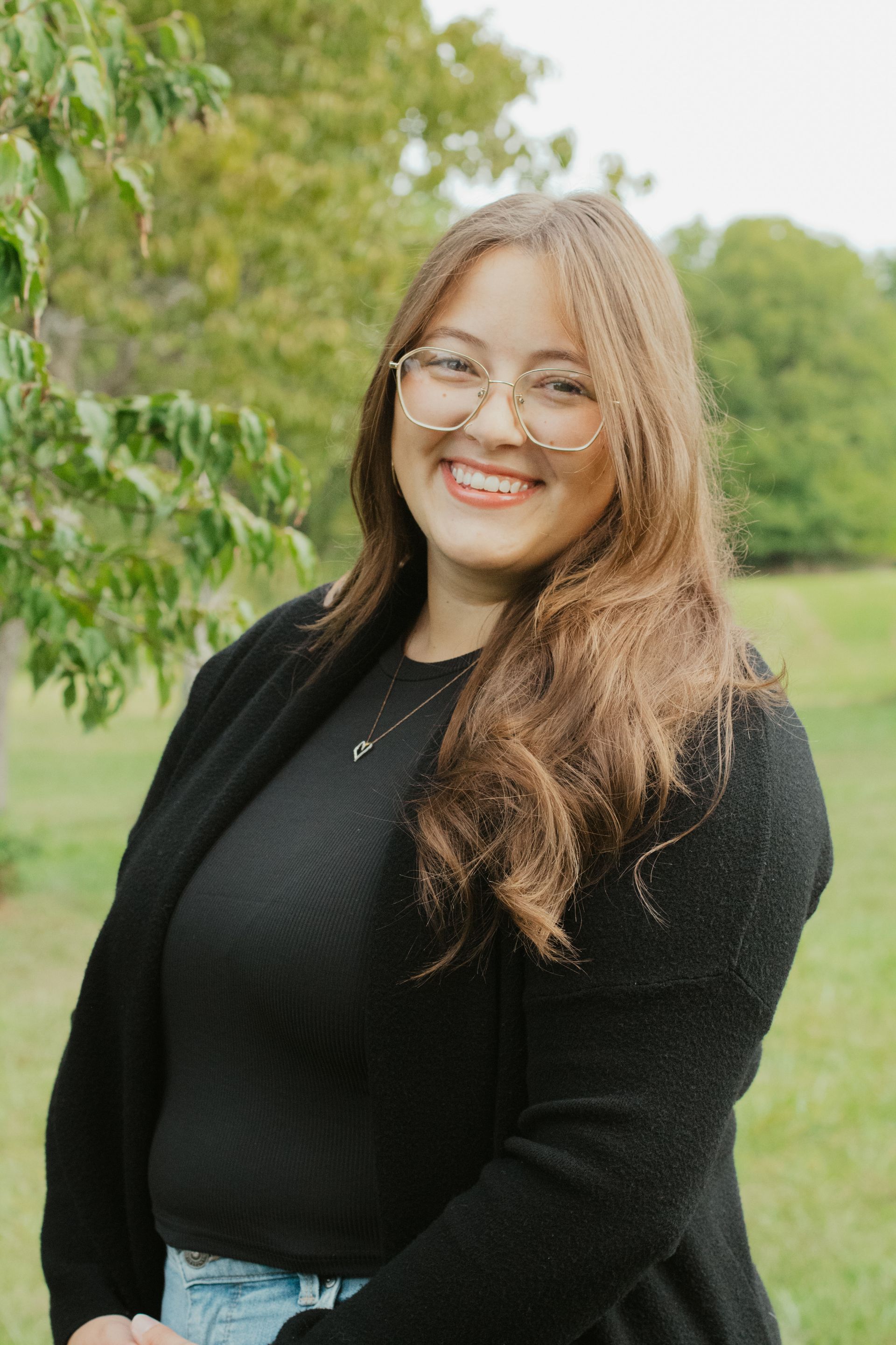 Woman with glasses smiles; sits in front of a brick wall, wearing a red sweater.