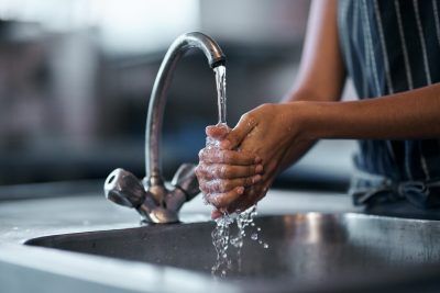 Person washing hands under a faucet in a kitchen sink. Water flowing, person wearing apron.