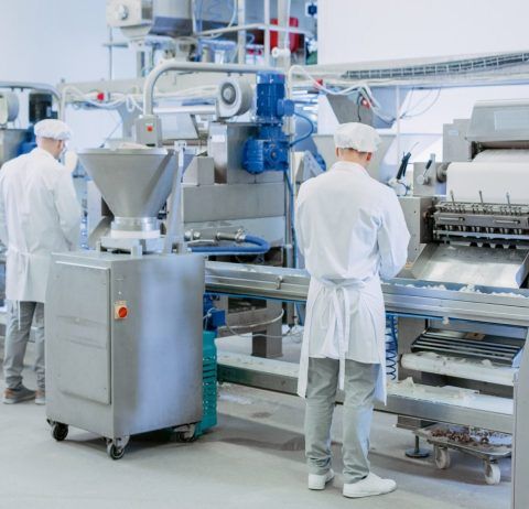 Two workers in white lab coats operating food processing machinery in a factory.