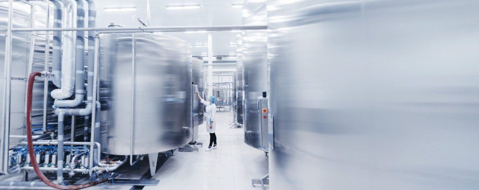 Inside a sterile factory with stainless steel tanks and a worker in a white coat.