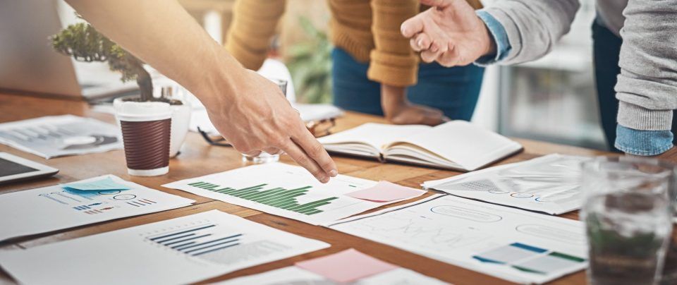 People pointing at and discussing charts on a table.