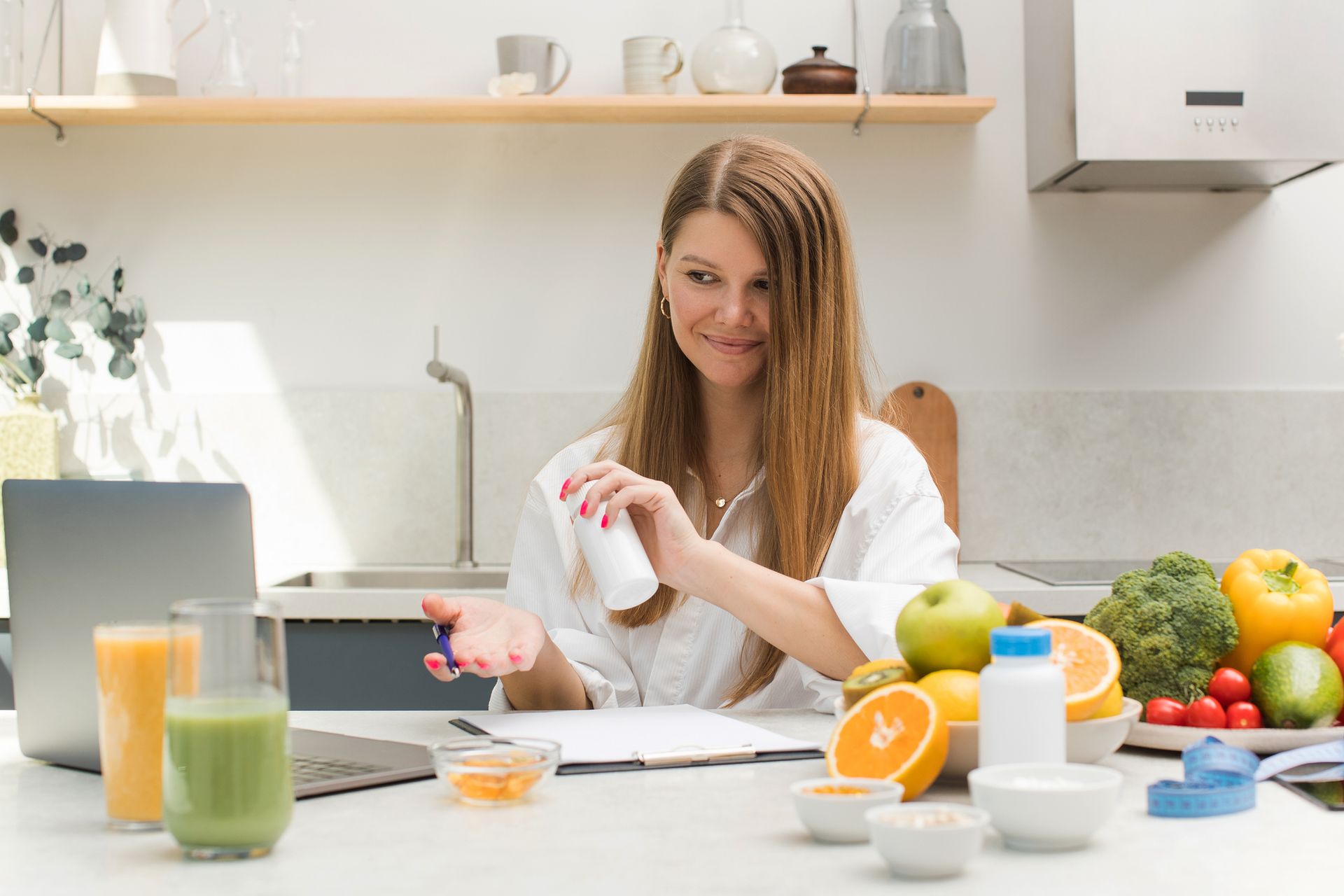 A woman is sitting at a table in a kitchen holding a bottle of yogurt.