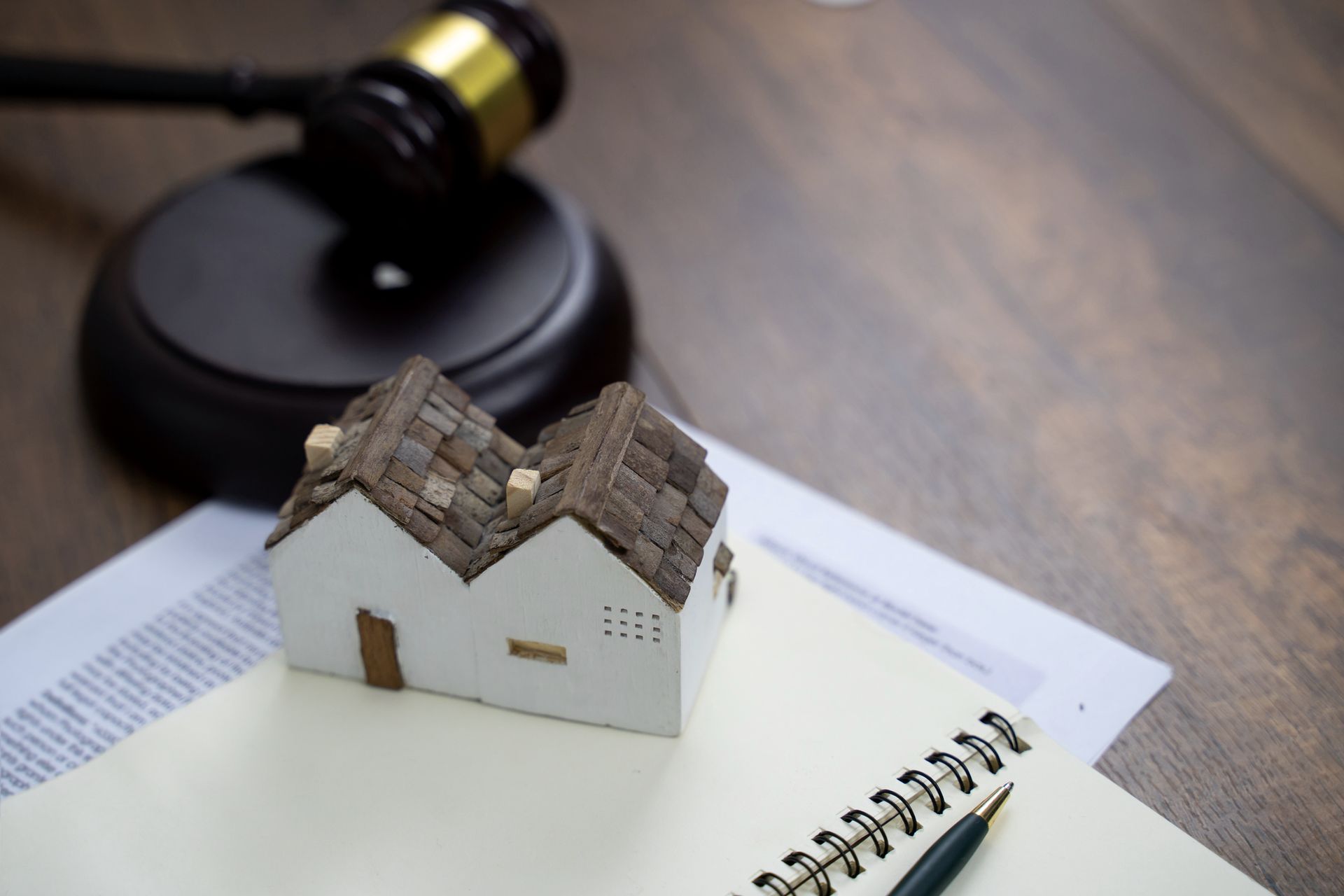 A model house is sitting on top of a notebook next to a judge 's gavel.