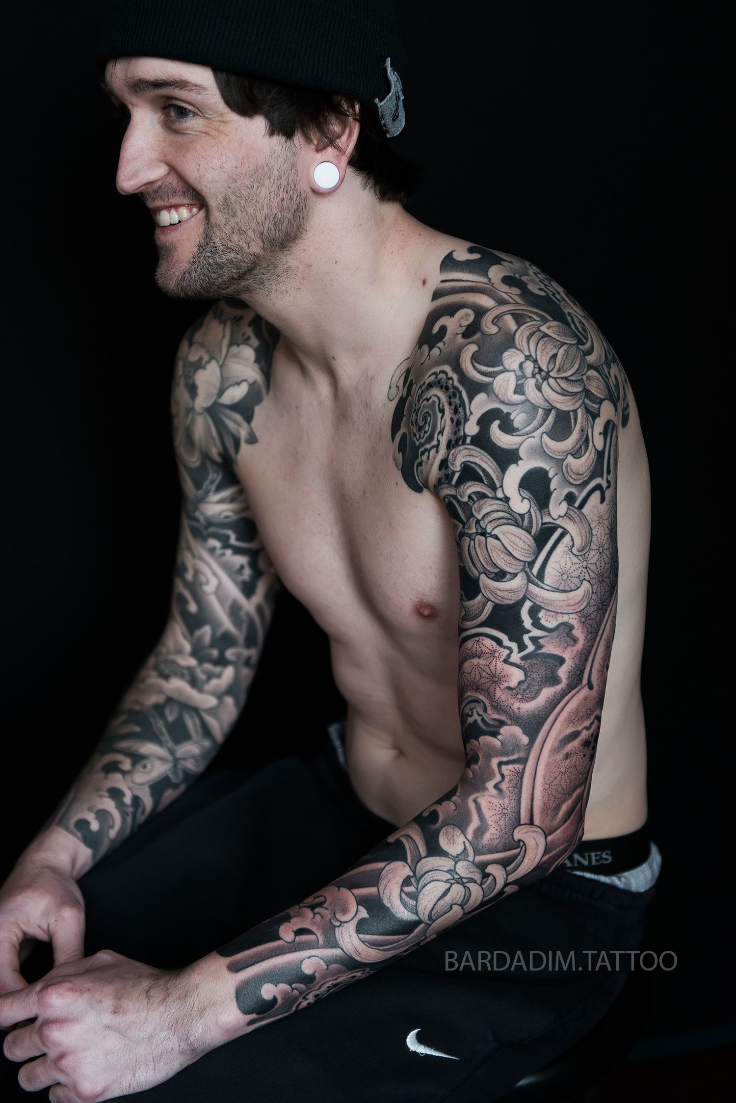 A shirtless man with a full sleeve tattoo on his arm