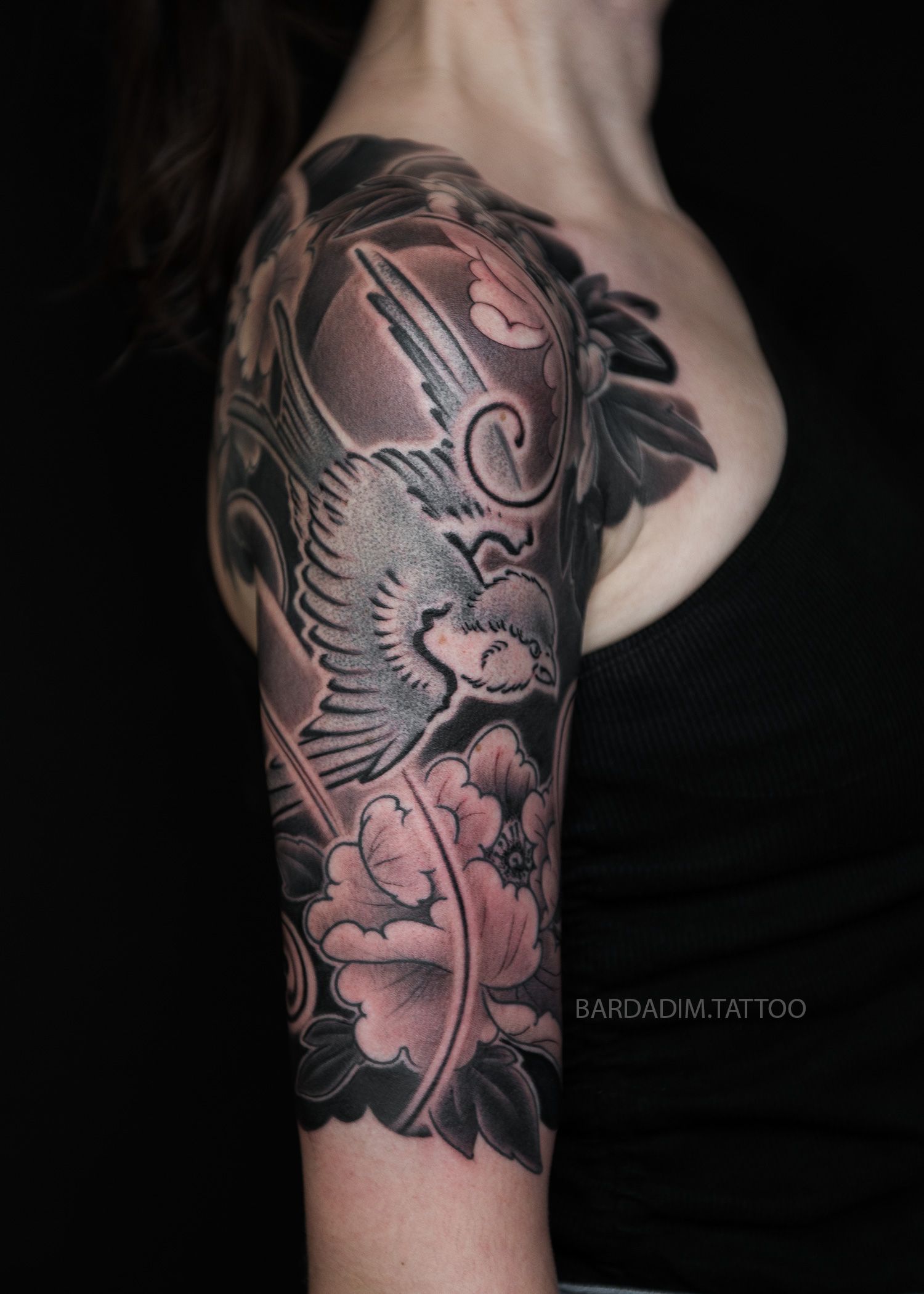 A woman has a tattoo of a bird and flowers on her arm