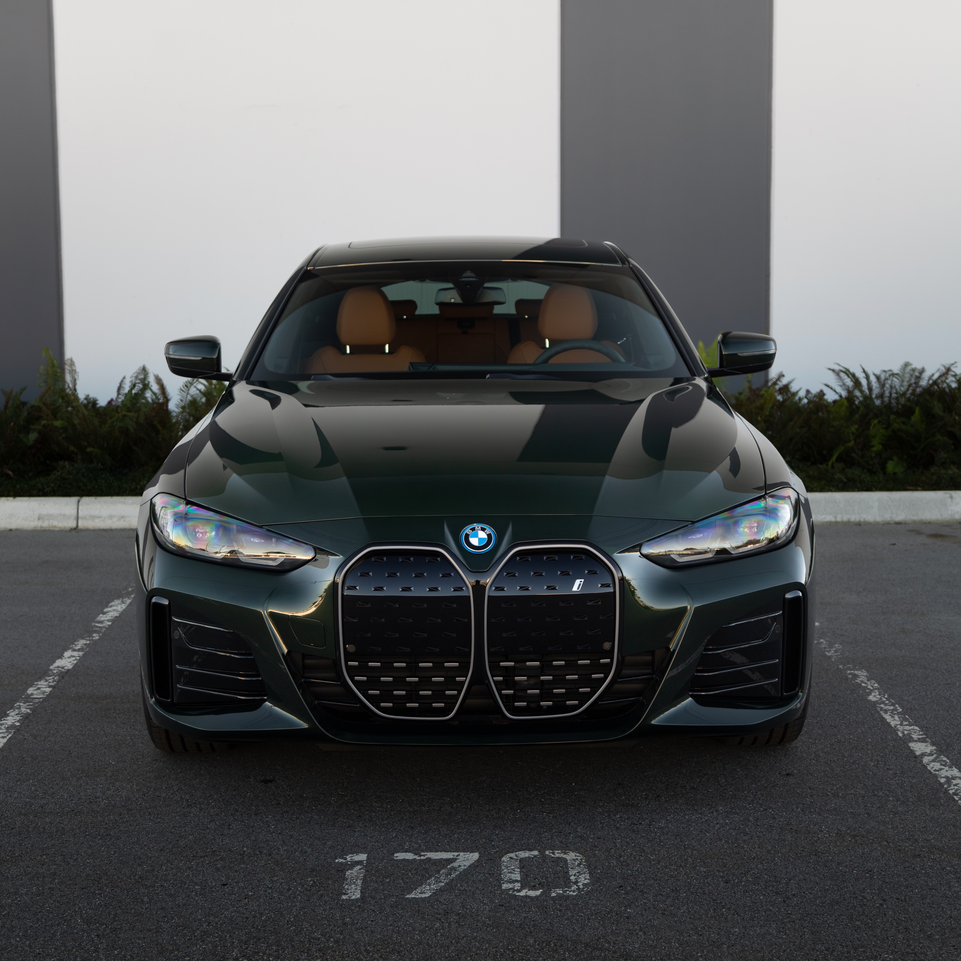 A blue bmw is parked in a parking lot in front of a building.