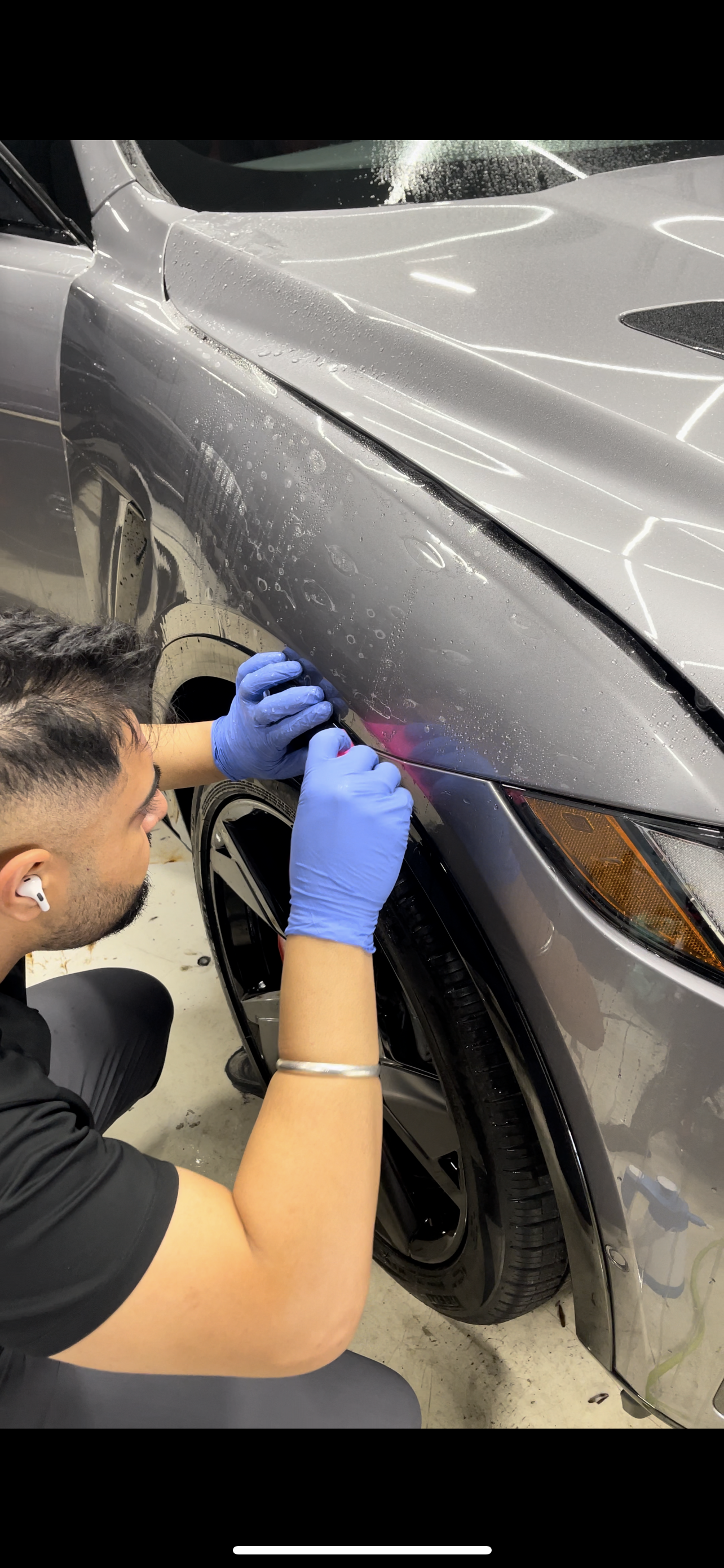A man wearing blue gloves is working on the side of a car.