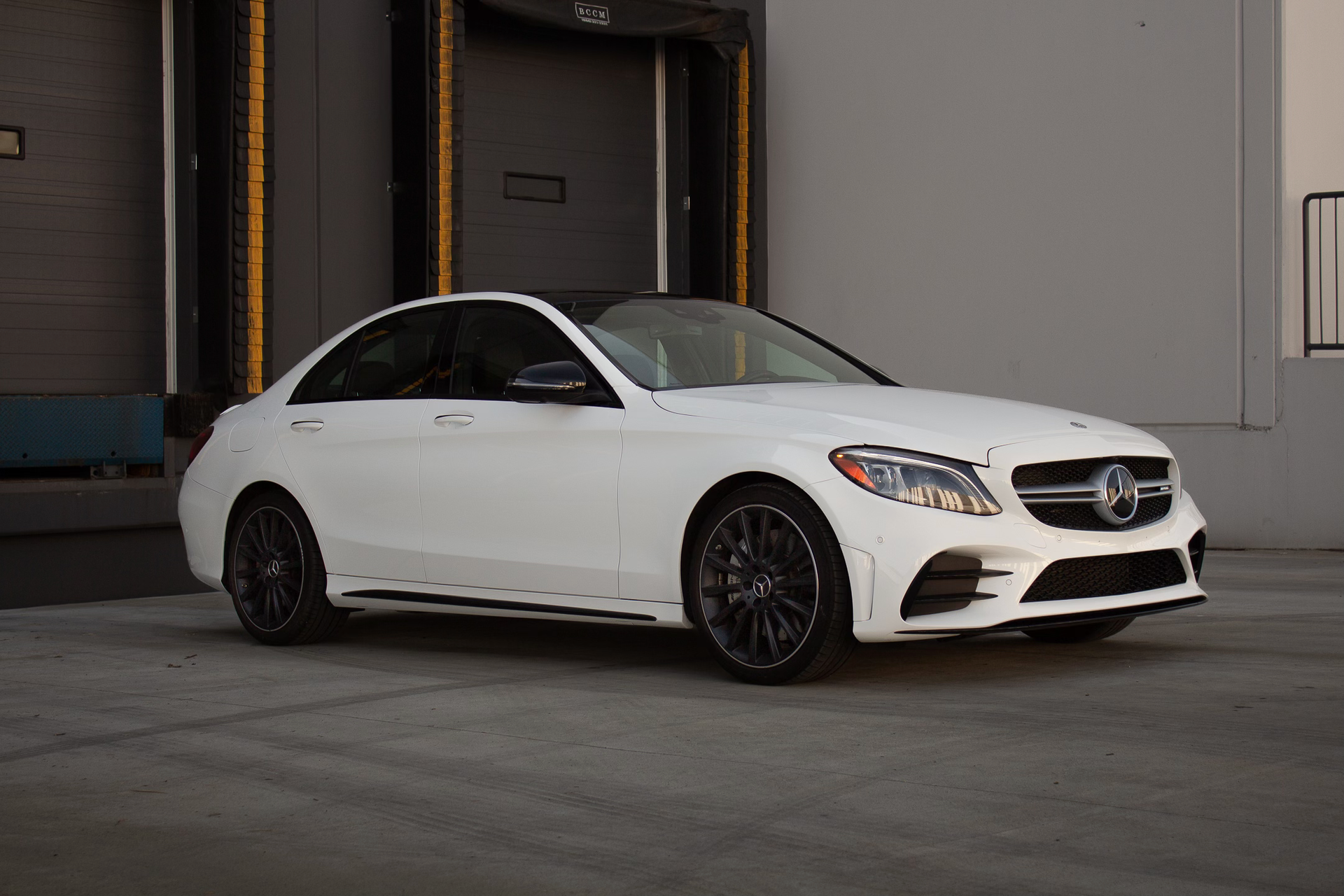 A white mercedes benz c class is parked in front of a building.