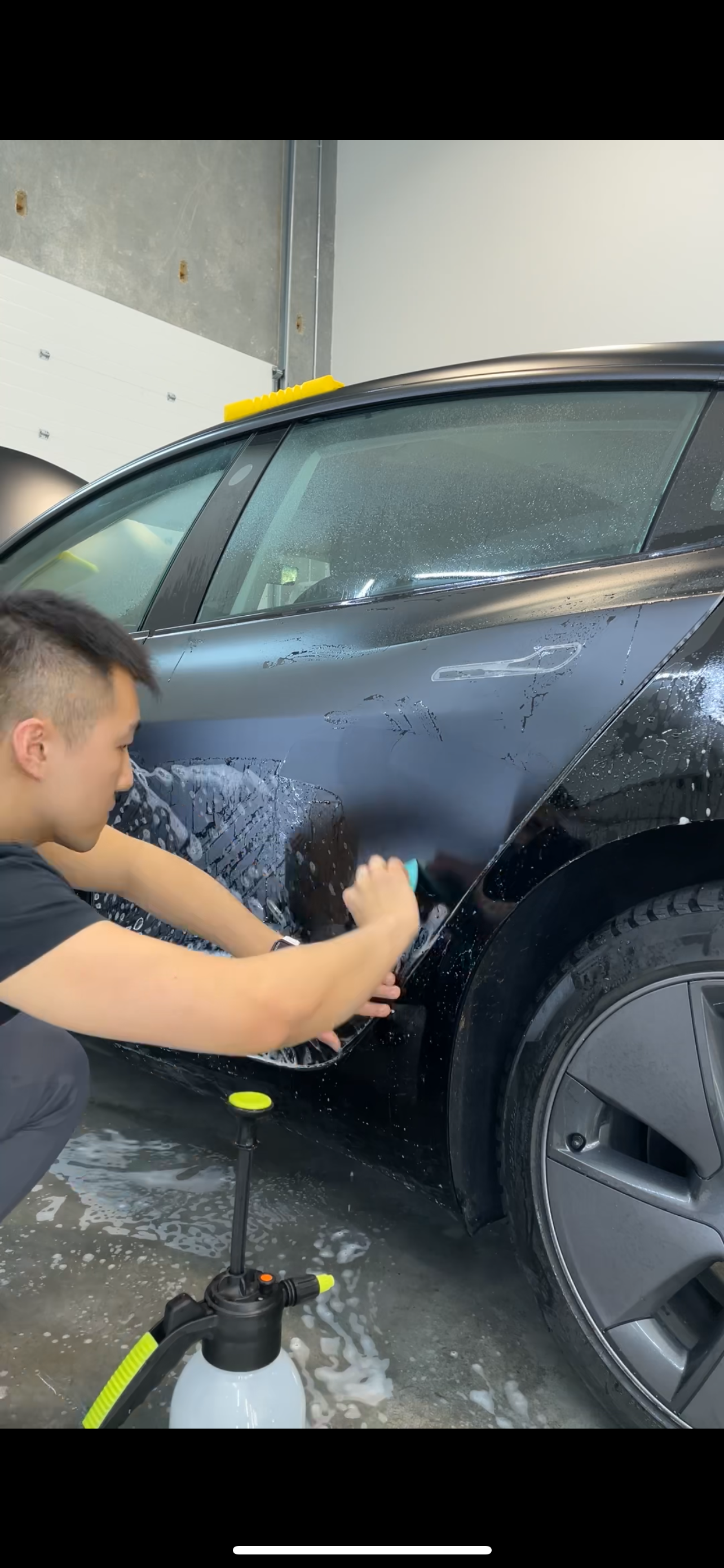 A man is washing a tesla model 3 in a garage.