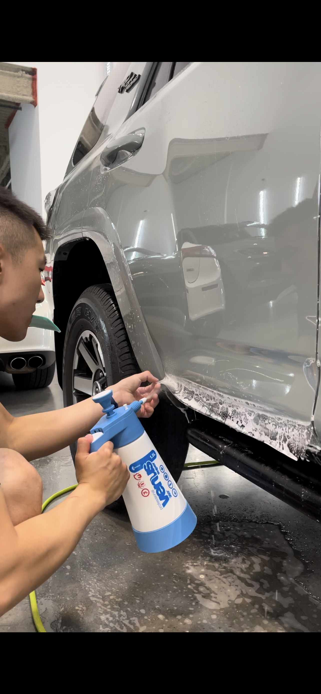A man is cleaning the side of a car with a spray bottle.