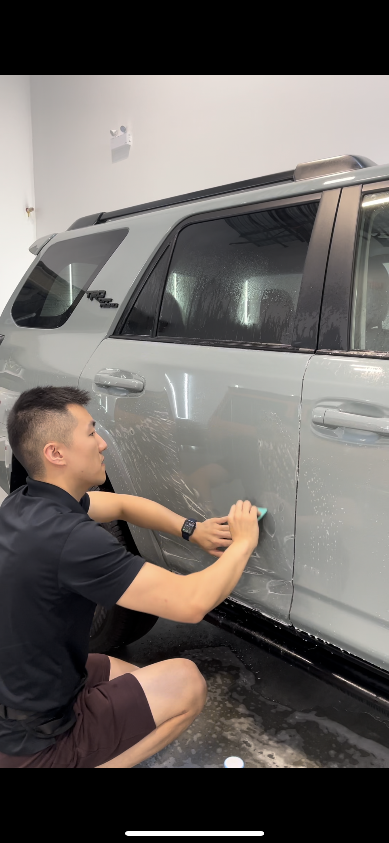 A man is kneeling down next to a gray suv.