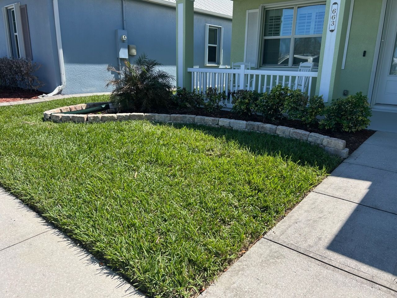 Small front yard with green grass, curved flower bed, and a concrete walkway beside a house
