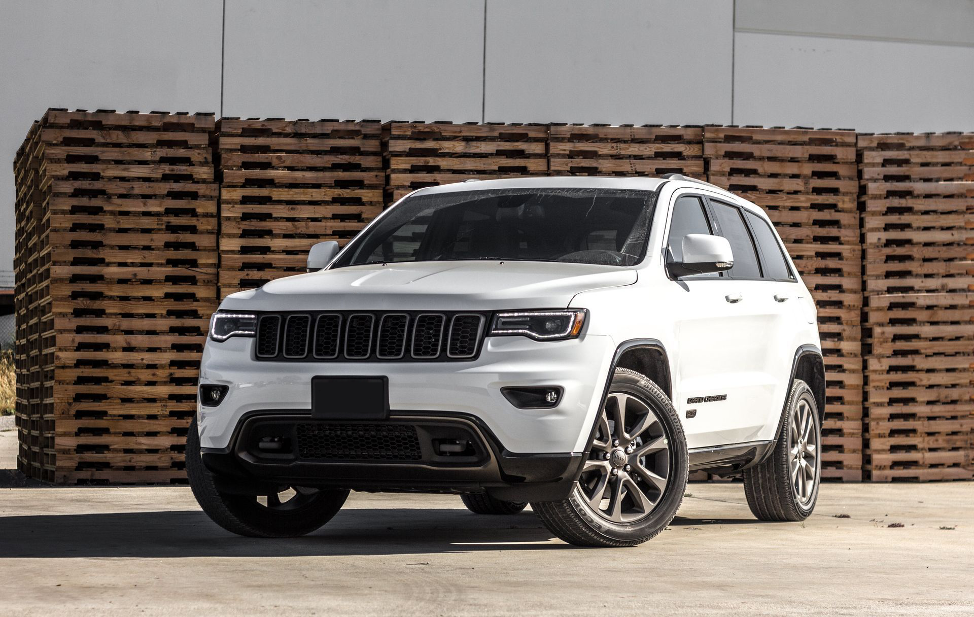 A white jeep grand cherokee is parked in front of a pile of wooden pallets.
