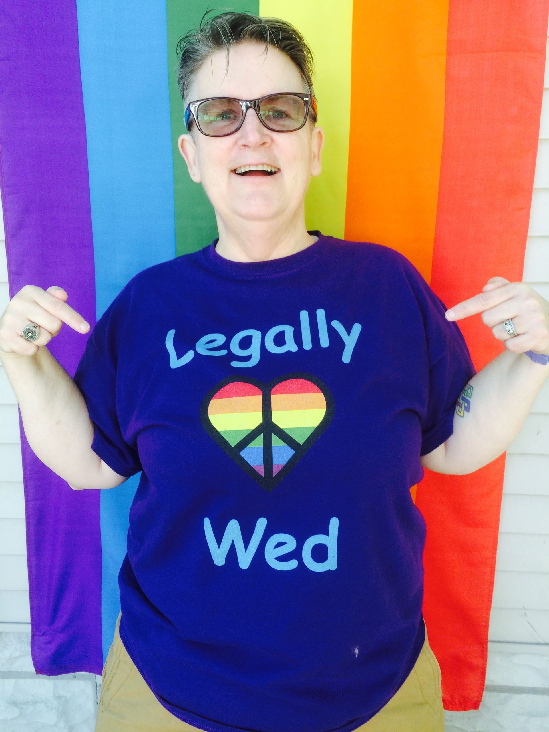 A person smiling and pointing to their purple t-shirt that says