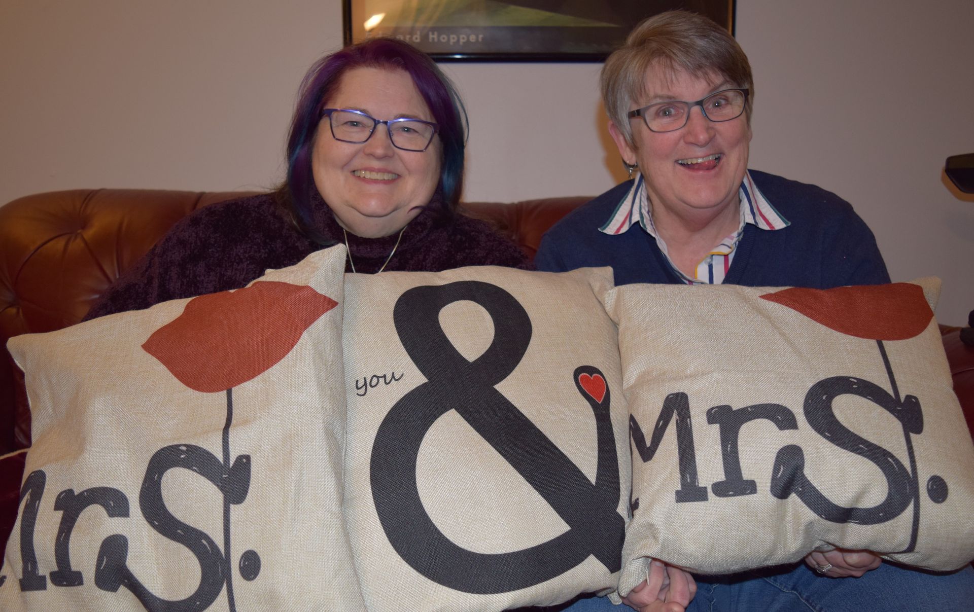 Two people smiling while holding three decorative pillows that spell out 
